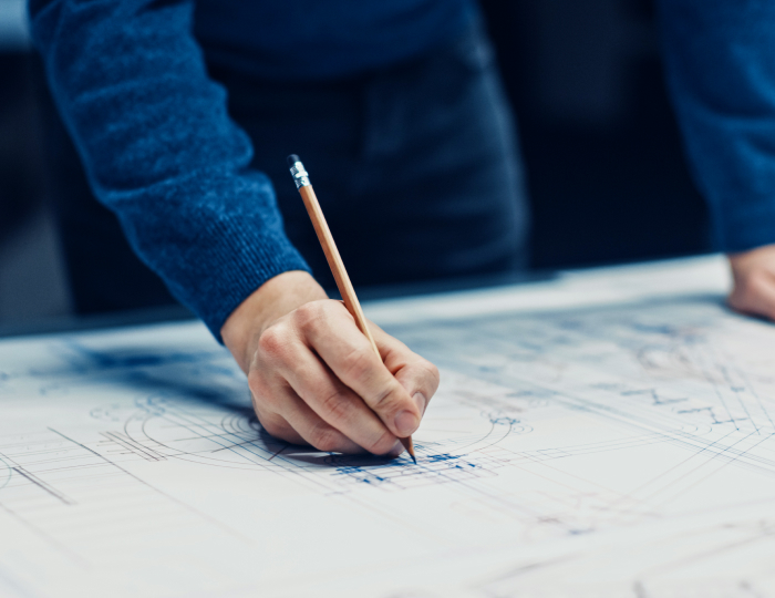 Close-up of a person's hand drawing technical aluminum designs on a blueprint with a pencil
